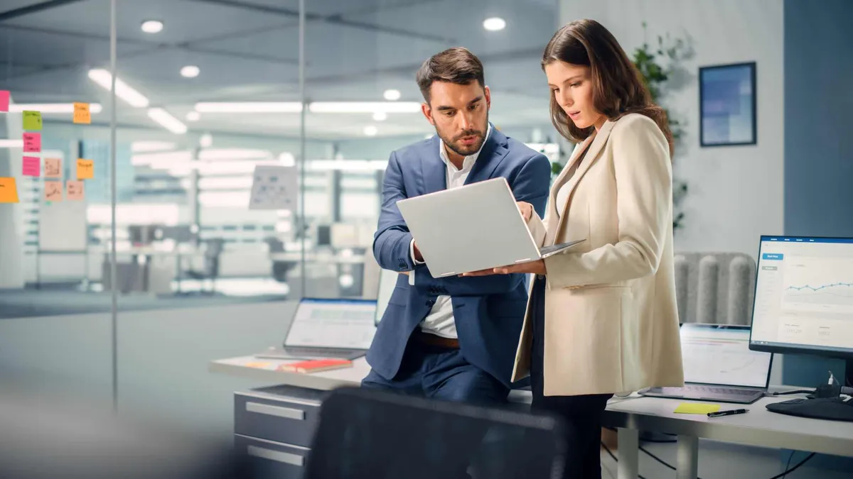 Dos profesionales revisan en una laptop los números de su empresa en una oficina