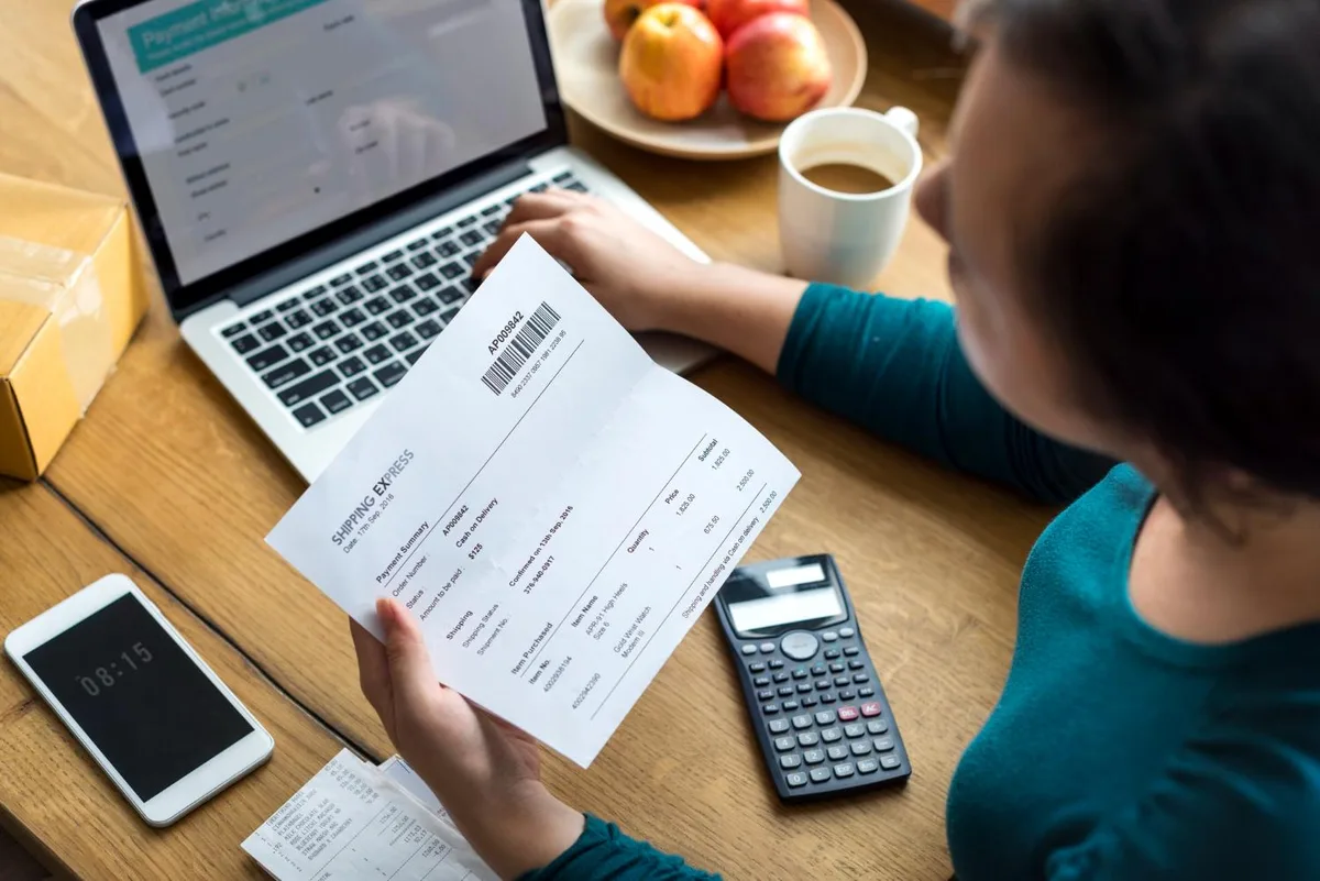 Persona revisando un remito de compra impreso junto a una notebook y una calculadora